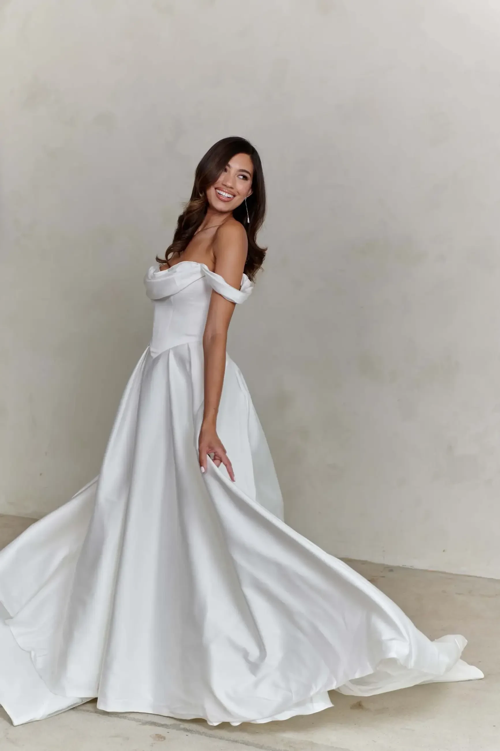 A woman in a white off-the-shoulder gown twirls gracefully, showcasing the flow of the dress.