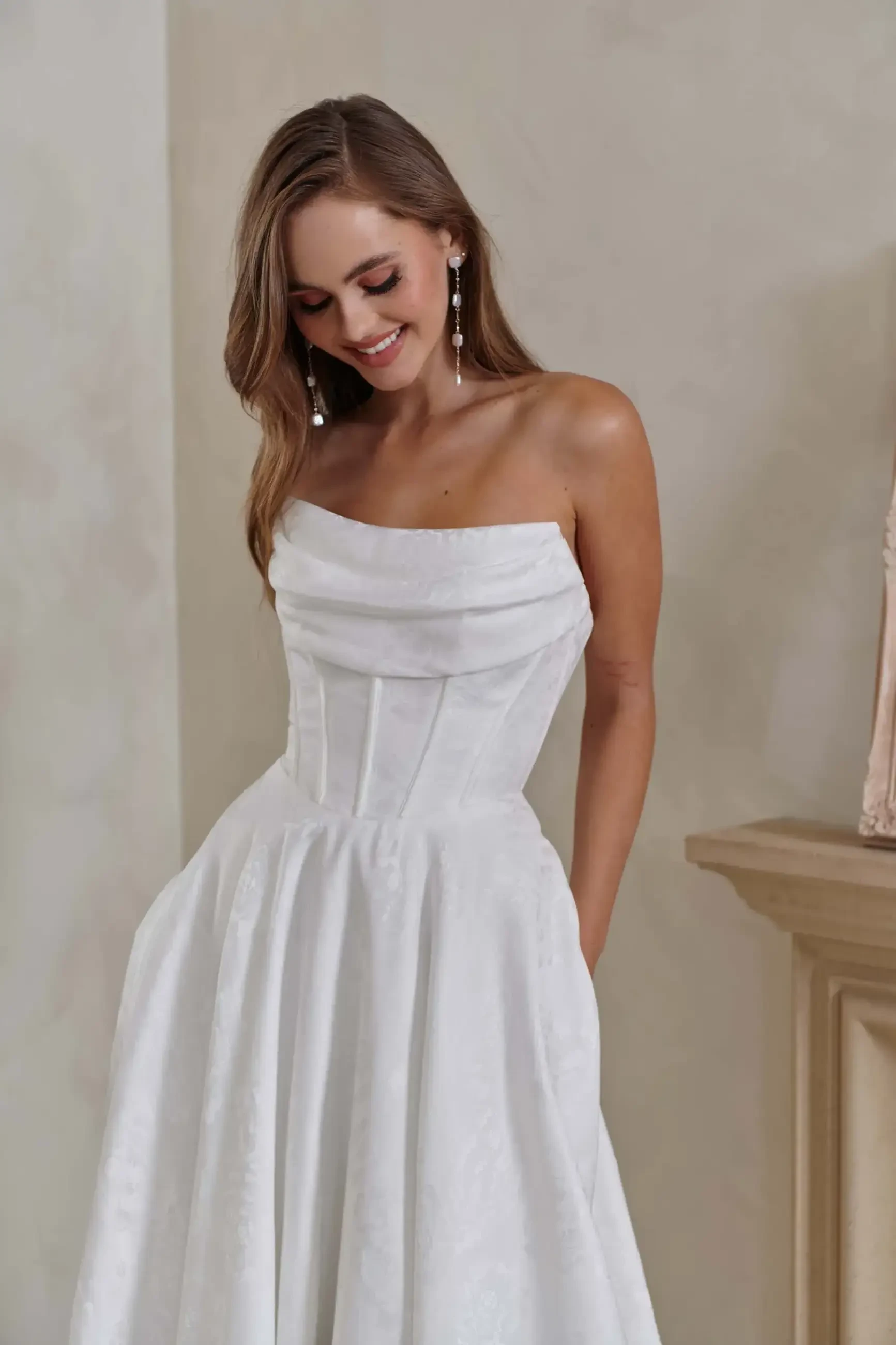 A woman in a strapless white dress standing and smiling.