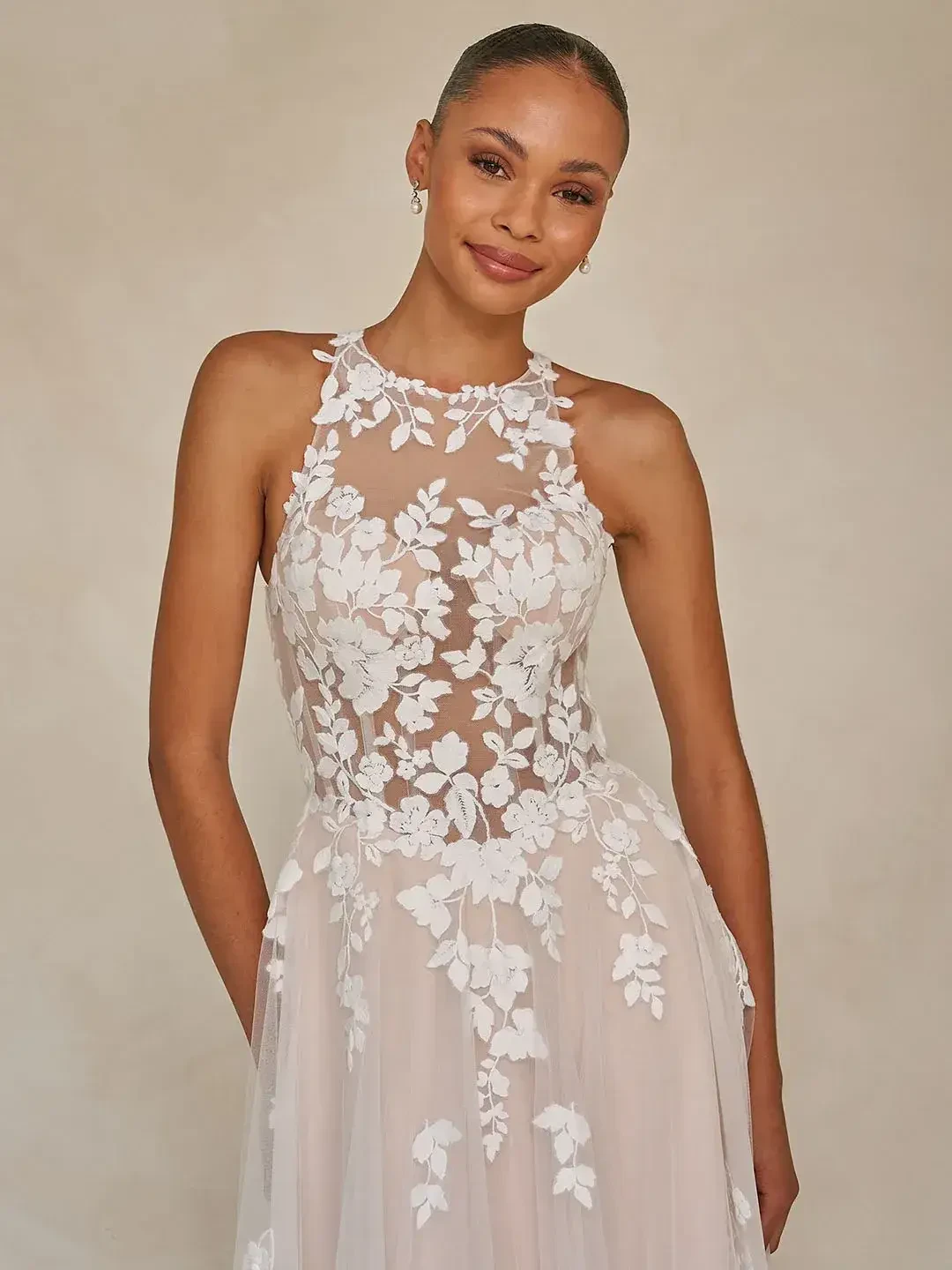 A woman in a sleeveless, floral-embroidered gown, smiling and posing elegantly.