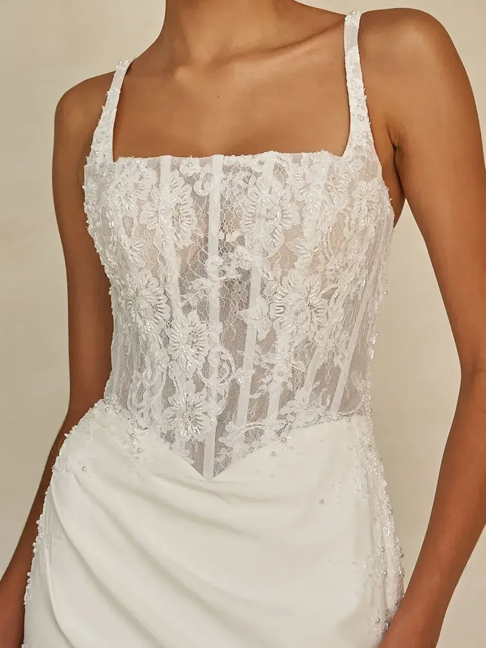 Woman wearing a sleeveless white lace corset wedding dress. The bodice features intricate floral lace patterns, creating an elegant and romantic look.